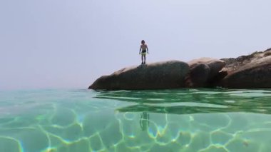 Çocuk bir kayadan denize atlıyor, derin ve derin bir çekimde yakalanıyor. Görüntüler onu suyun altına dalarken ve kristal berraklığında turkuaz suda yüzerken izliyor..