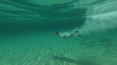 Çocuk bir kayadan denize atlıyor, derin ve derin bir çekimde yakalanıyor. Görüntüler onu suyun altına dalarken ve kristal berraklığında turkuaz suda yüzerken izliyor..