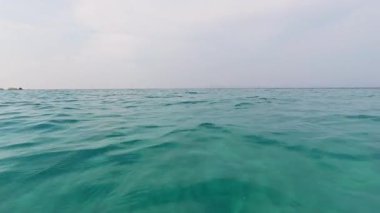 Sakin bir günde hafif deniz dalgalarının yavaş çekim görüntüsü. Temiz turkuaz su, yumuşak bir gökyüzünün altında ufka kadar uzanıyor. Huzur ve sükuneti çağrıştırıyor..