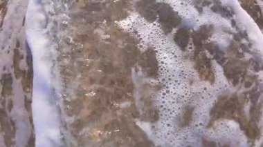 Okyanus köpüğünün yavaşça kumsaldaki ıslak kumun üzerinden geçerek rahatlatıcı ve huzurlu bir doğal şablon oluşturduğu yavaş çekim videosu. Sahil şeridi hareketinin yakın çekim görüntüsü.