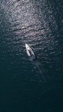Bir yelkenlinin parlak güneş ışığı altında derin mavi denizde yüzüşünün üst görüntüsü. Suyun parlak yansımaları huzurlu, manzaralı bir deniz atmosferi yaratır..