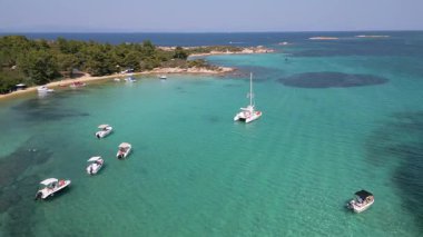 Kumlu sahil ve çam ormanı yakınlarındaki kristal berraklığında turkuaz suya demirlenmiş katamaran ve küçük teknelerin hava manzarası. Akdeniz kıyısındaki Idyllic yaz sahnesi.