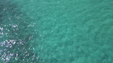 Kristal berraklığında turkuaz deniz suyunun görünür dokuları ve hafif dalgalanmalarla yakın çekim görüntüsü. Tasarım, seyahat ve yaz temalı içerik için mükemmel doğal arkaplan.