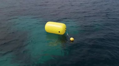 Sakin mavi denizde yüzen sarı bir şamandıranın videosu, dalgalarla yavaşça sallanıyor. Güvenli, seyrüsefer ve açık deniz teması için ideal bir deniz manzarası..