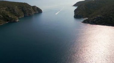 İki yemyeşil yarımada arasında sakin bir deniz kanalından geçen bir teknenin hava görüntüsü. Güneşli bir günde doğaya, suya ve özgürlüğe huzurlu ve manzaralı bir bakış..