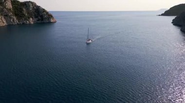 İki yemyeşil yarımada arasında sakin bir deniz kanalından geçen bir teknenin hava görüntüsü. Güneşli bir günde doğaya, suya ve özgürlüğe huzurlu ve manzaralı bir bakış..