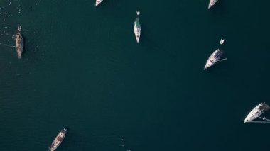 Durgun mavi denize demir atmış birden fazla yelkenlinin hava videosu. Yukarıdan aşağıya görünüm, seyahat, yaşam tarzı ve deniz temaları için ideal minimum ve geometrik bir deniz kompozisyonu yaratır.