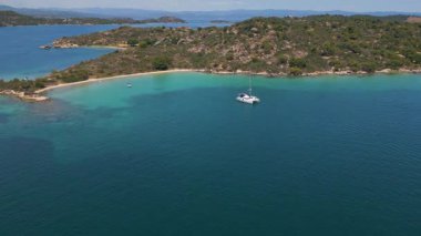 Çapalı tekneleri, kayalık kıyı şeridi ve turkuaz sığ suları olan sakin bir hangarın havadan görüntüsü. Yumuşak tepeleri ve kumlu plajı olan huzurlu Akdeniz manzarası.