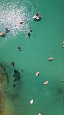 Kıyıya yakın sığ turkuvaz sularda demirli teknelerin hava manzarası. Açık deniz, yüzücüler ve yaz atmosferi yukarıdan rahatlatıcı ve canlı bir sahil atmosferi yaratır..