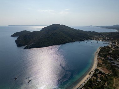 Çapalı yelkenli ve yemyeşil tepeli huzurlu bir körfez manzarası. Sakin deniz güneş ışığını yansıtır, sakin ve manzaralı bir kıyı manzarası yaratır..