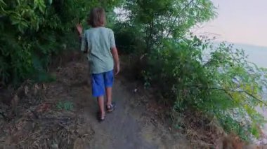 Dar bir orman yolunda yeşil ağaçlar ve yaz bitkileriyle çevrili beton adımlarla yürüyen bir çocuğu izleyen birinci şahıs POV. Ormanda barışçıl doğa keşfi.