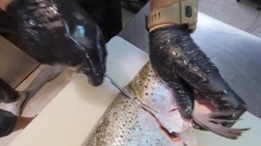 Beyaz kesim tahtasındaki bıçakla taze alabalık doğrayan şefin yakın çekimi. Ticari mutfakta profesyonel deniz ürünleri hazırlığı.