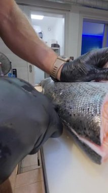 Beyaz kesim tahtasındaki bıçakla taze alabalık doğrayan şefin yakın çekimi. Ticari mutfakta profesyonel deniz ürünleri hazırlığı.