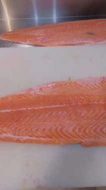 Profesyonel bir mutfakta kesme tahtasında taze çiğ somon filetosu yakın plan. Temiz hazırlık ve pembe balık etinin canlı dokusu.