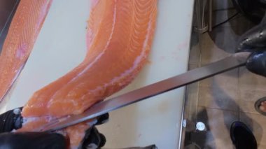 Şef, profesyonel bir mutfakta taze somon fileto dilimliyor. Siyah eldivenli ve çiğ balık desenli eller..