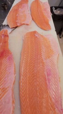 Profesyonel bir mutfakta kesme tahtasında taze çiğ somon filetosu yakın plan. Temiz hazırlık ve pembe balık etinin canlı dokusu.