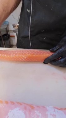 Şefin taze somon filetosundan çivi kemiklerini cımbızla çıkardığı yakın plan. Eller siyah eldivenlerle profesyonel mutfakta balık hazırlıyor..