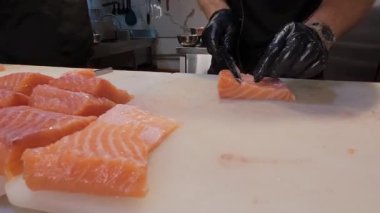 Şef, profesyonel bir mutfakta taze somon fileto dilimliyor. Siyah eldivenli ve çiğ balık desenli eller..