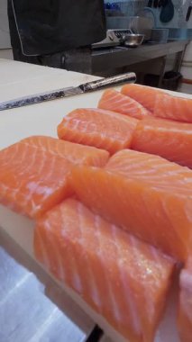 Şef, profesyonel bir mutfakta taze somon fileto dilimliyor. Siyah eldivenli ve çiğ balık desenli eller..