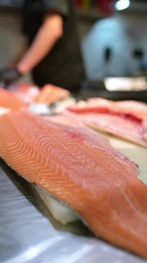 Şef, profesyonel bir mutfakta taze somon fileto dilimliyor. Siyah eldivenli ve çiğ balık desenli eller..