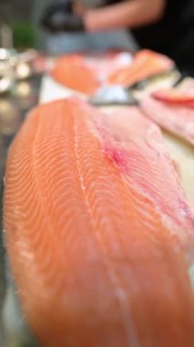 Şef, profesyonel bir mutfakta taze somon fileto dilimliyor. Siyah eldivenli ve çiğ balık desenli eller..