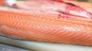 Profesyonel bir mutfakta kesme tahtasında taze çiğ somon filetosu yakın plan. Temiz hazırlık ve pembe balık etinin canlı dokusu.