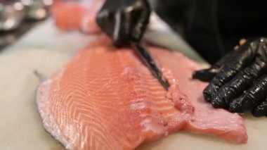 Şef, profesyonel bir mutfakta taze somon fileto dilimliyor. Siyah eldivenli ve çiğ balık desenli eller..