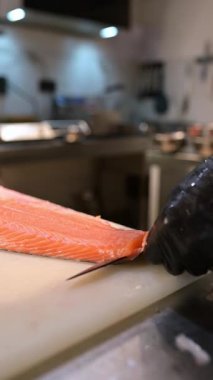 Şef, profesyonel bir mutfakta taze somon fileto dilimliyor. Siyah eldivenli ve çiğ balık desenli eller..