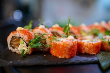Tobiko, krema sosu ve mikroyeşilliklerle kaplı lezzetli suşi dürümleri Japon restoranındaki siyah bir tabağa dizilmişti..
