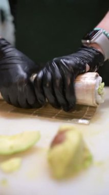 Şef, somon, avokado, ton balığı ve yılan balığı katmanlı suşi rulosu hazırlıyor. Profesyonel mutfakta bambu hasırı kullanılıyor..