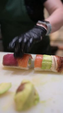 Şef, somon, avokado, ton balığı ve yılan balığı katmanlı suşi rulosu hazırlıyor. Profesyonel mutfakta bambu hasırı kullanılıyor..