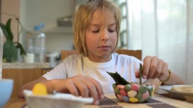 Küçük bir çocuk kahvaltı masasında yosun yiyor. Doğal ışık ve rahat ev atmosferiyle sağlıklı bir sabah rutini..