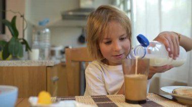 Küçük çocuk sıcak mutfakta kahvaltı masasında süt içiyor. Doğal ışık ve sağlıklı yiyeceklerle huzurlu bir sabah rutini..