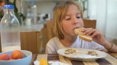 Küçük bir çocuk kahvaltı masasında sade ekmek yiyor. Doğal ışık ve basit ev yapımı yiyeceklerle huzurlu bir sabah rutini..