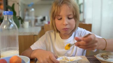 Genç bir çocuk kahvaltı masasında çatalla taze meyve yiyor. Doğal ışık ve sağlıklı yiyeceklerle huzurlu bir sabah ortamı..