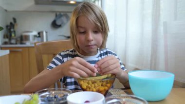 Evde yemek masasında fıstık yiyen küçük bir çocuk. Doğal ışık, gevşemiş ruh hali ve sağlıklı çerez içeren rahat ve rahat bir mutfak..