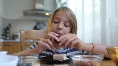 Evde mutfak masasında kremalı tatlı yiyen küçük bir çocuk. Rahat bir atmosfer, doğal ışık, rahat ortamlarda tatlı süt ürünleri ikram edilen günlük atıştırma zamanı..