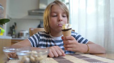 Evdeki mutfak masasında dondurma yiyen küçük bir çocuk. Doğal ışık, rahat atmosfer, tatlı muamele ve günlük hayattaki neşeli an..