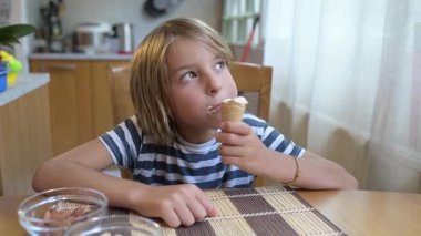 Evdeki mutfak masasında dondurma yiyen küçük bir çocuk. Doğal ışık, rahat atmosfer, tatlı muamele ve günlük hayattaki neşeli an..