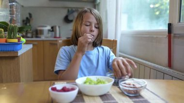 Evde yemek masasındaki bir kaseden yabanmersini toplayan küçük bir çocuk. Doğal gün ışığı, rahat bir atmosfer, sıcacık mutfakta meyveli ve fındıklı sağlıklı atıştırmalıklar..