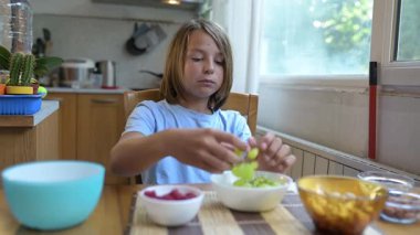 Evde yemek masasında yeşil üzüm yiyen küçük bir çocuk. Doğal ışık, gevşek mutfak seti, fındık ve böğürtlenli sağlıklı meyve aperatifi.