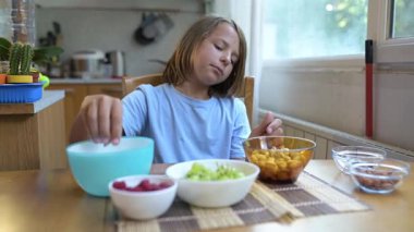 Evde yemek masasında fıstık yiyen küçük bir çocuk. Doğal ışık, gevşemiş ruh hali ve sağlıklı çerez içeren rahat ve rahat bir mutfak..