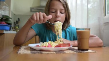 Küçük bir çocuk mutfak masasında taze sebzelerle spagetti yiyor. Sıcak atmosfer, doğal ışık, sağlıklı öğle yemeği ve her gün içilen içki..