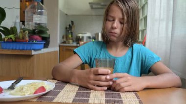 Küçük çocuk sıcak mutfakta kahvaltı masasında süt içiyor. Doğal ışık ve sağlıklı yiyeceklerle huzurlu bir sabah rutini..