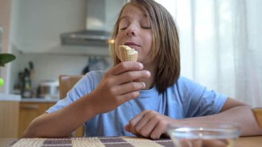 Evdeki mutfak masasında dondurma yiyen küçük bir çocuk. Doğal ışık, rahat atmosfer, tatlı muamele ve günlük hayattaki neşeli an..