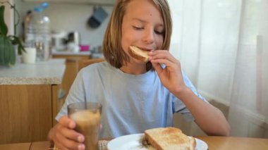 Küçük bir çocuk kahvaltı masasında sade ekmek yiyor. Doğal ışık ve basit ev yapımı yiyeceklerle huzurlu bir sabah rutini..
