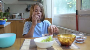 Evde mutfak masasında ahududu yiyen küçük bir çocuk. Doğal gün ışığı, sağlıklı meyve çerezi, basit ve rahat bir aile ortamı..
