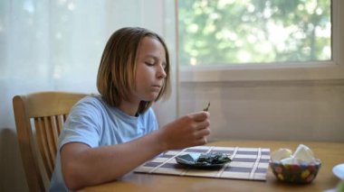 Küçük bir çocuk kahvaltı masasında yosun yiyor. Doğal ışık ve rahat ev atmosferiyle sağlıklı bir sabah rutini..