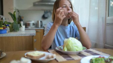 Küçük çocuk mutfak masasında taze marul yiyor. Doğal ışık, sağlıklı vejetaryen atıştırmalık, basit ve sıradan günlük atmosfer..