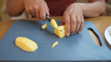 Mutfakta çiğ patatesi dilimleyen bir kadın. Ev yapımı yemekler pişirmek için taze sebzeler hazırlıyorum. Patatesleri bıçakla kesen ellerin yakın çekimi..